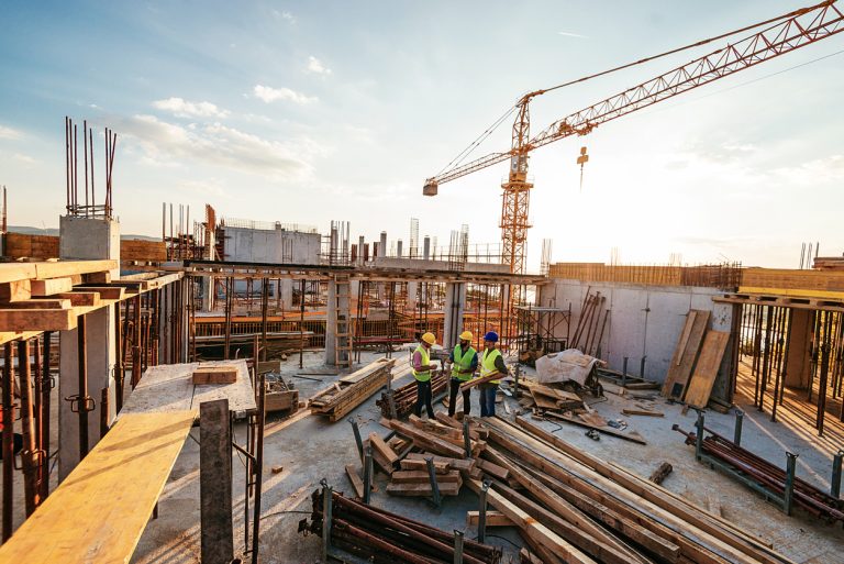 architects and engineers discussing work progress between concrete walls, scaffolds and cranes.