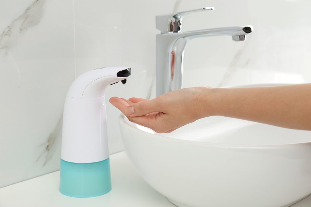 close-up of person using touchless bathroom faucet and soap dispenser