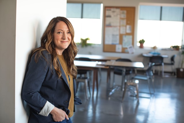 Female teacher standing at entrance to classroom (classroom behind her is out of focus)