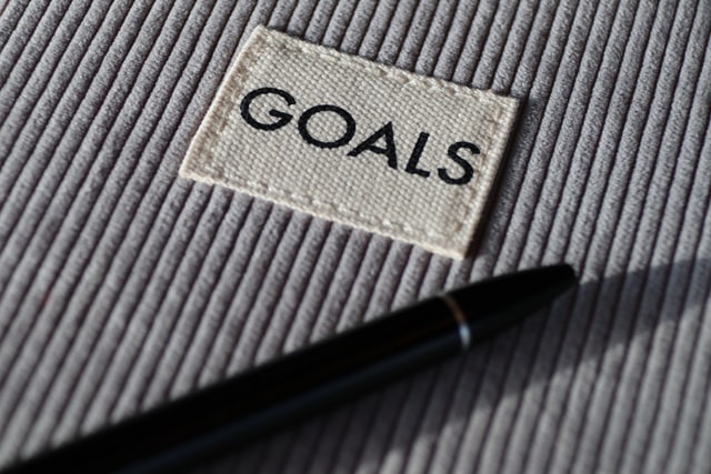 cloth label reading "GOALS" and pen on burlap textured background