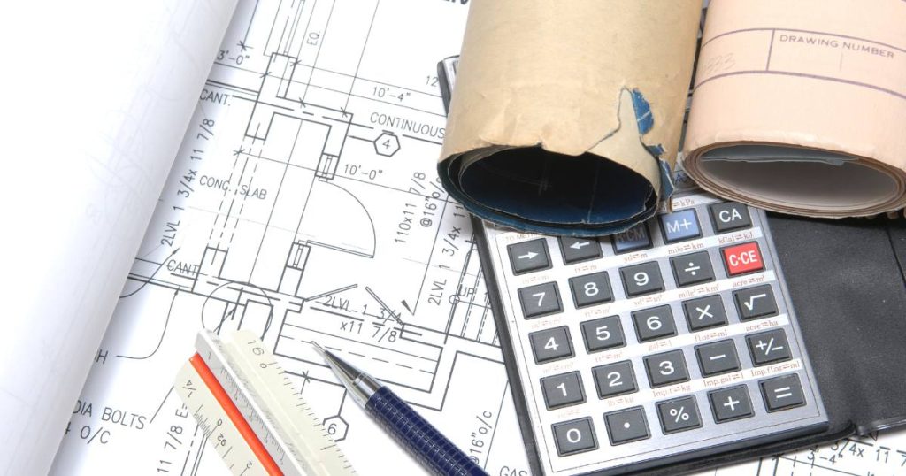 Table covered in construction plans and budget documents.